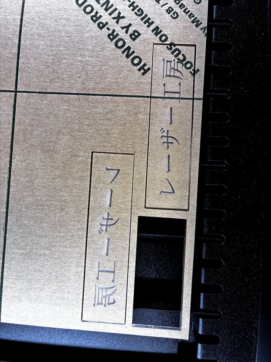 レーザー加工機の中。加工が終わったアクリル板。保護紙が貼られたままで、切り抜いた部分が抜けている